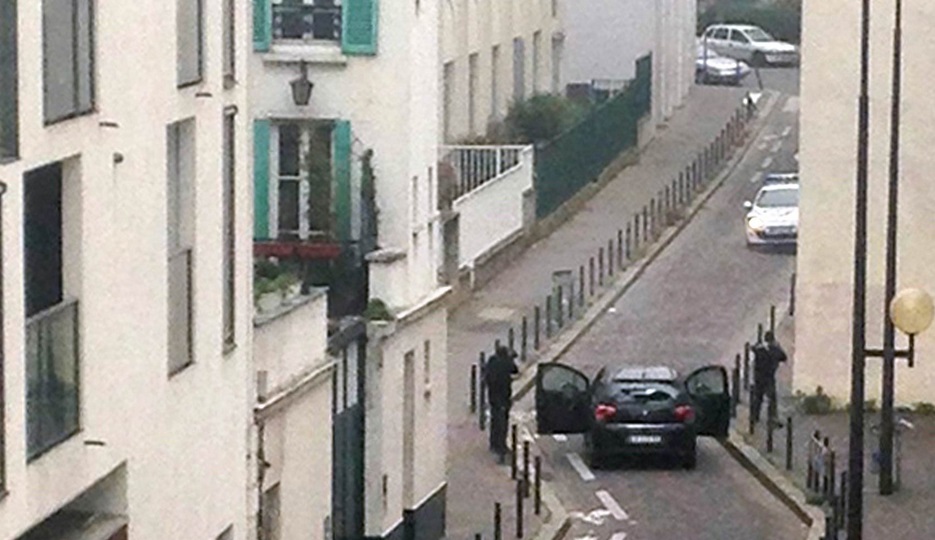 Homens armados são vistos saindo de um carro e apontando armas a um carro da polícia perto do escritório da revista satírica 'Charlie Hebdo' (Crédito: Anne Gelbard/AFP)